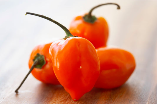 A pile of orange habanero peppers on a wooden cutting board.