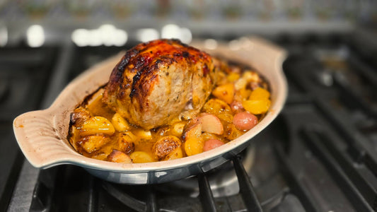 A pork roast on a bed of potatoes, in a two-handled casserole dish.